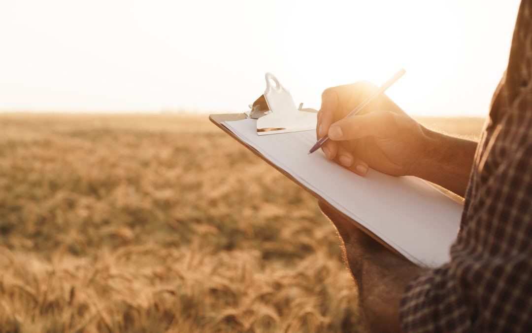 Man taking notes on his clipboard while standing in front of a field