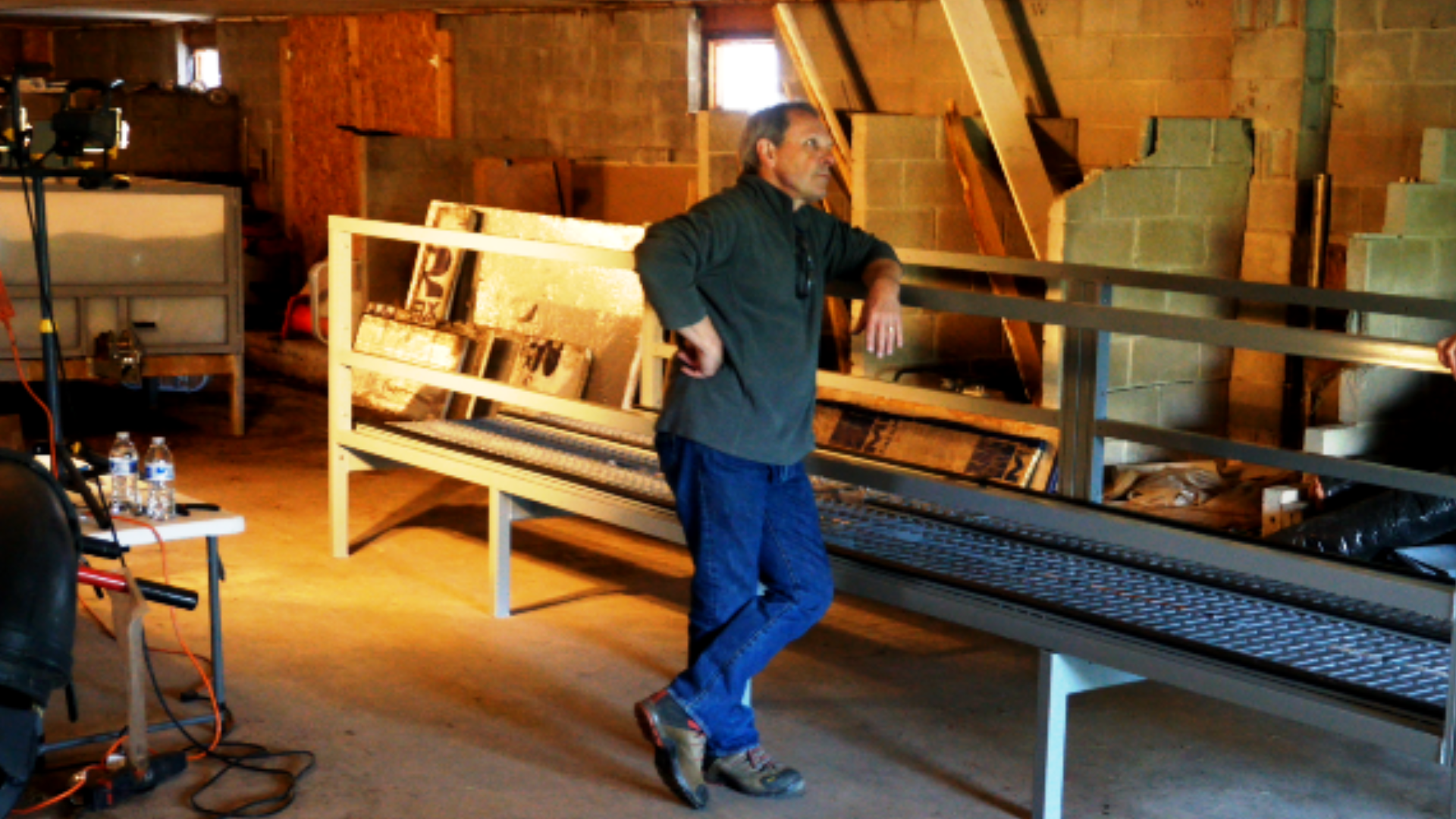Image showing Dan Lonowski standing beside a partially constructed Wormgear continuous flow-through (CFT) composting system, inside a work-in-progress building with construction and agricultural equipment around.