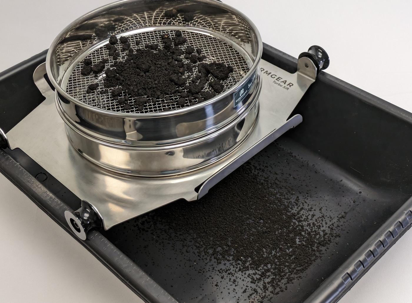 A Wormgear Turbo Sift sieve on its steel plate across a black tub, with finished dark compost sifted into the tub below.